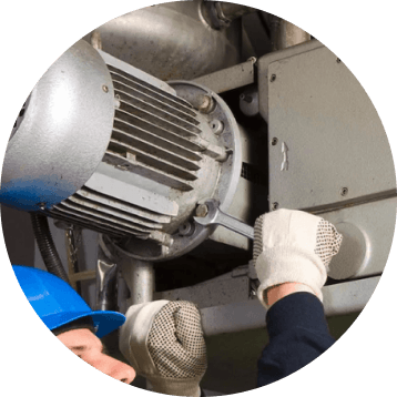 A person in a blue hard hat and white gloves servicing an industrial electric motor and fan.